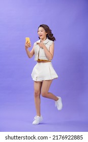 Excited cheerful woman holding cell phone in hand pointing at screen mobile jumping up over purple background - Shutterstock ID 2176922885