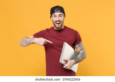 Excited Cheerful Young Bearded Tattooed Guy In Casual T-shirt Black Cap Point Index Finger On Laptop Pc Computer Isolated On Yellow Background Studio. Mockup Copy Space. Tattoo Translate Life Is Fight