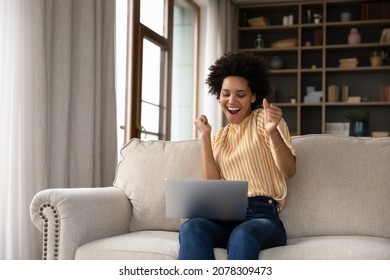 Excited cheerful young Black woman using laptop computer on sofa at home, getting good news, feeling joy, dancing with hands, singing, laughing, making winner gesture, happy to win prize - Shutterstock ID 2078309473