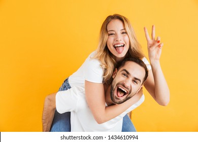 Excited cheerful young couple standing isolated over yellow background, piggyback ride, peace gesture - Powered by Shutterstock