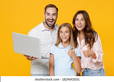 Excited Cheerful Young Parents Mom Dad With Child Kid Daughter Teen Girl In Basic T-shirts Using Laptop Pc Computer Showing Thumbs Up Isolated On Yellow Background Studio Portrait. Family Day Concept