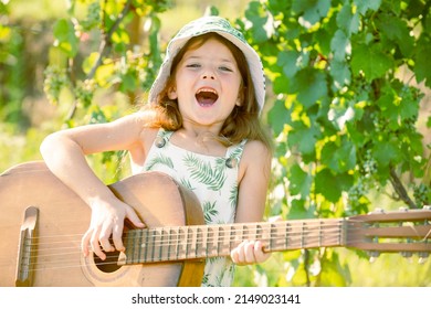 Excited Child Musician Playing The Guitar Like A Rockstar. Smiling Child Playing Outdoors In Summer.