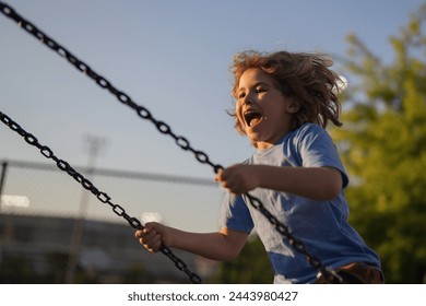 Excited child swinging on chain swing on city kids playground. Swing ride. Cute child having fun on a swing on summer sky background. Blonde little boy swings at kid playground. Child swinging high. - Powered by Shutterstock