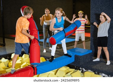 Excited children boy and teen girl having funny wrestling by inflatable logs while celebrating birthday in leisure sport center for kids