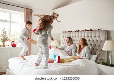 Excited Children Jumping On Parents Bed At Home As Family Open Gifts On Christmas Day