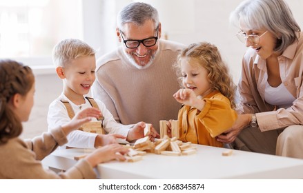 Excited children playing game Jenga at home with positive senior grandparents while sitting on sofa in living room, two little girls and boy spending happy time with grandma and grandpa on weekend