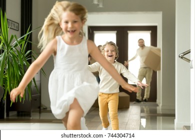 Excited Children Running On Camera, Funny Little Girl And Boy Having Fun Playing Happy To Move In New Own Big Modern House, Young Family With Kids And Cardboard Boxes Entering Home At Moving Day 