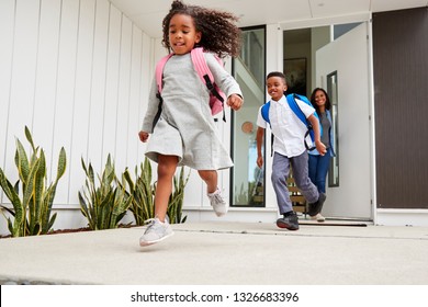 Excited Children Running Out Of Front Door On Way To School Watched By Mother