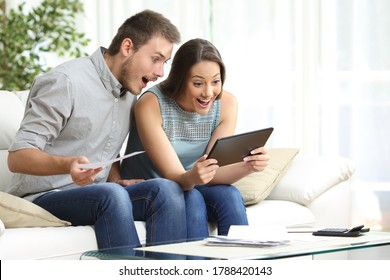 Excited couple checking tablet and receipts sitting in the sofa in the living room at home