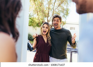 Excited couple at entrance door with bottle of wine. Friends being welcomed by couple at the door. Attending friend's housewarming party.