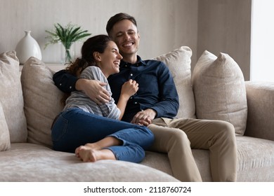 Excited Couple Hugging, Relaxing Sitting On Couch Having Fun Together, Happy Beautiful Girlfriend And Boyfriend Spending Leisure Time Lazy Weekend At Home, Talking And Laughing At Funny Joke