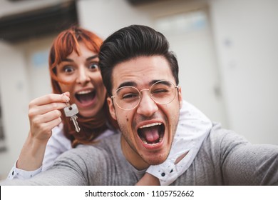 Excited couple with keys to their new home hugging and looking at camera taking selfie - Powered by Shutterstock