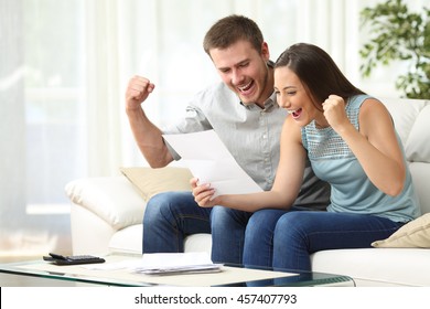 Excited couple reading a letter together sitting on a sofa in the living room at home
