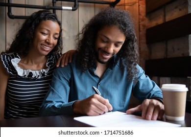 Excited couple sit in coffee shop sign paper document make agreement, happy African American  man and woman close deal with wedding planner or consultant in cafe - Powered by Shutterstock