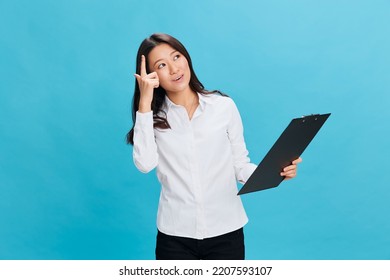 Excited Cute Asian Businesswoman In Classic Office Dress Code Holds Folder Tablet With Resume Point Finger Up Posing Isolated On Over Blue Studio Background. Cool Business Offer. Job Interview Concept