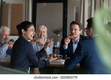 Excited diverse employees eating pizza during break in office together, happy Indian businesswoman laughing at funny joke, talking chatting with colleagues, having fun, sharing corporate lunch - Shutterstock ID 2032893779