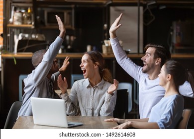 Excited diverse friends celebrate online win watch football game on laptop sit at cafe table together, overjoyed multicultural young football fans supporters happy with victory goal score at party - Powered by Shutterstock