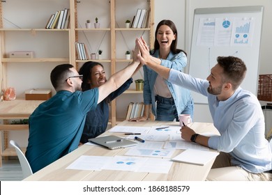 Excited diverse multiethnic employees have fun give high five engaged in teambuilding activity at meeting. Happy overjoyed multiracial colleagues celebrate shared team business success or victory.