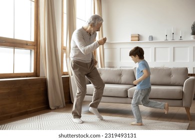 Excited elderly grandfather have fun dance with little preschooler grandson in living room at home. Overjoyed mature granddad enjoy family weekend listen to music with small 6s boy child. - Powered by Shutterstock