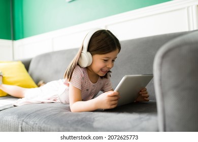 Excited elementary kid relaxing on the couch while watching online videos or movies on the tablet at home - Powered by Shutterstock