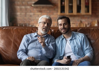 Excited engaged grown son and senior father watching movie, football match on TV sport channel together, sitting on couch in living room with remote control, enjoying leisure, having fun - Powered by Shutterstock