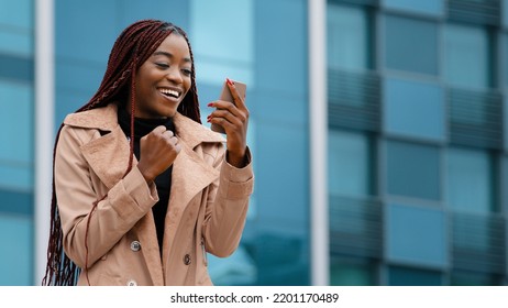 Excited enthusiastic surprised young woman winner standing outdoors reading good news on phone celebrating victory rejoicing in success winning lottery receives notification on smartphone side view - Shutterstock ID 2201170489