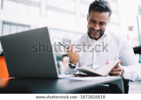 Excited entrepreneur 40s dressed in white shirt satisfied with business results, happy Caucasian male proud CEO with personal planner celebrating projecting goal sitting at sidewalk table with netbook