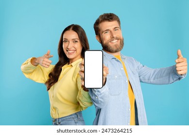 Excited European couple in casual holding and pointing at blank smartphone screen, demonstrating app or website on blue background, mockup - Powered by Shutterstock