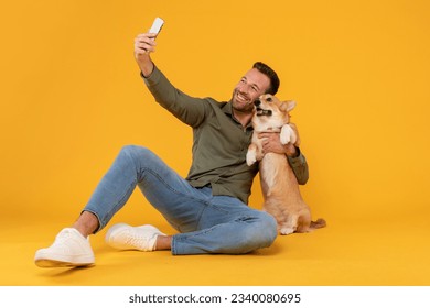 Excited european man taking selfie with his pretty corgi dog, posing looking at phone camera embracing pet, isolated on yellow studio background wall - Powered by Shutterstock