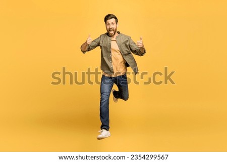 Excited european middle aged man running towards camera, smiling and showing thumb up over yellow studio background, full length, free space