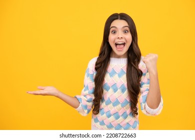 Excited Face. Portrait Of Cute Teenager Child Girl Pointing Hand Showing Adverts With Copy Space Over Yellow Background. Amazed Expression, Cheerful And Glad.