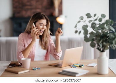 Excited Fair-haired Woman Smiling Widely While Having A Phonecall And Raising Hand Triumphantly