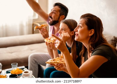 Excited Family cheering for their sport team on TV, Eating pizza in the living room at home. Fans with hands up and pizza slices in hands having fun watching favorite game on Television. Copy space - Powered by Shutterstock