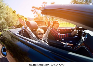 aufgeregte Zweierfamilie, junger Vater und sein lächelnder Sohn mit Händen hoch in der Luft, genussreiche Straße in Cabrio Auto, Reise- und Urlaubskonzept, Sonnenflare