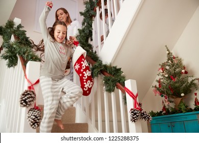 Excited Family Wearing Pajamas Running Down Stairs Holding Stockings On Christmas Morning