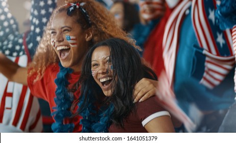 Excited Fans With US Flag In Sports Crowd Celebrating On Team Success. Group Of American Soccer Fans Cheering In Stands.