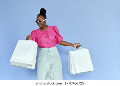 Excited fashion stylish young african american woman shopaholic shopper wear pink blouse and sunglasses holding shopping bags looking inside isolated on lilac violet studio background. Fashion sale.