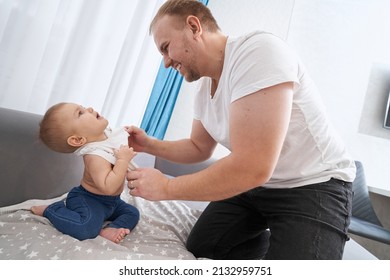 Excited Father Dressing Baby In T-shirt On Sofa