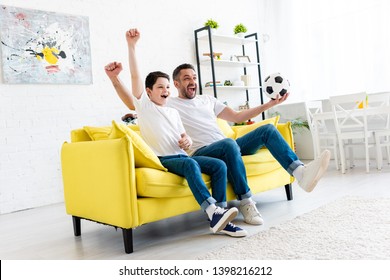 excited father and son cheering and watching sports match on couch in Living Room