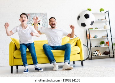 excited father and son cheering while watching sports match in Living Room
