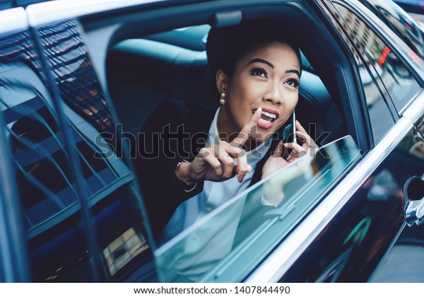 Excited female director pointing somewhere while
communicating with company colleague via mobile phone connected to
roaming internet, successful woman passenger spending congestion
time for cell call