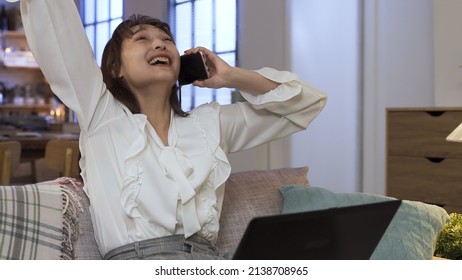 Excited Female Entrepreneur Clenching Fist While Responding To Business Victory On Phone. On The Sofa In Pleasure. Genuine Lifestyle