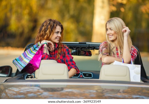 Excited female friends with shopping bags in\
convertible car. woman driving and shopping with girl friends.\
shopping bags happy and excited on road trip travel vacation in\
convertible car in\
summer.