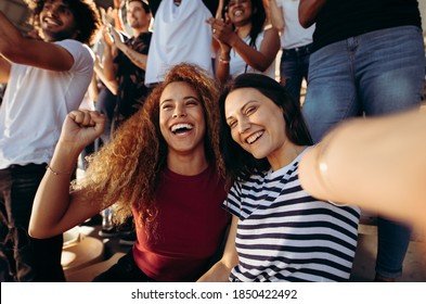 Excited female spectators making a selfie while cheering their sports team from a stadium. Cheerful men and woman fans taking selfie while watching match in stadium. - Shutterstock ID 1850422492