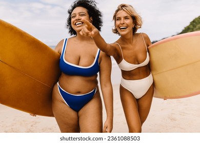 Excited female surfers going to a fun surfing spot on the beach, anticipating a happy and memorable surfing session. Two sporty women walking on shore in bikinis, eager to catch the best waves. - Powered by Shutterstock