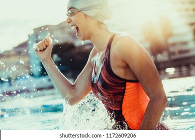 Excited female swimmer with clenched fist celebrating victory in the swimming pool. Woman swimmer cheering success in pool wearing swim goggles and cap. - Powered by Shutterstock