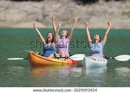 Excited friends celebrating vacation raising arms in kayaks in a lake