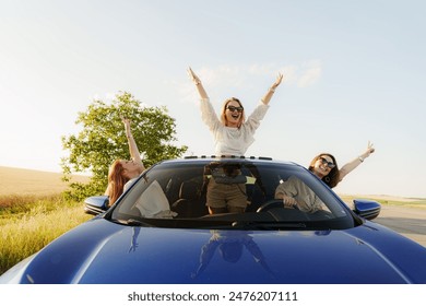 Excited friends with raised hands enjoying a road trip in a convertible car on a sunny day, embodying freedom and happiness. - Powered by Shutterstock