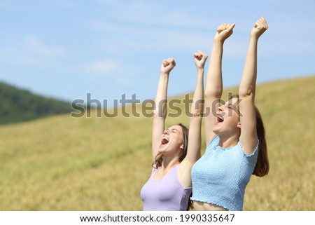 Excited friends raising arms celebrating vacation in a wheat field