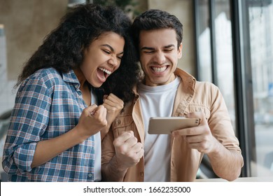 Excited Friends Using Smartphone, Playing Video Games. Happy Emotional Couple Celebration Success. Portrait Of Overjoyed Online Lottery Winners Looking At Digital Screen. Sport Betting Concept 